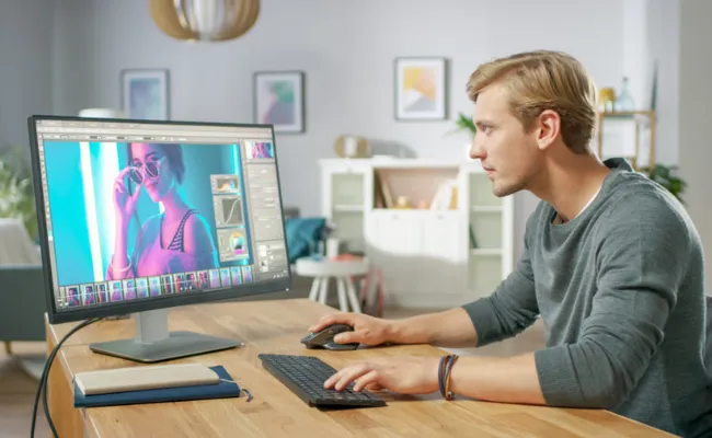 Young male editor enhancing a portrait using advanced photo editing software, showcasing professional photo retouching and color correction services as part of comprehensive video post-production services by a video editing company.