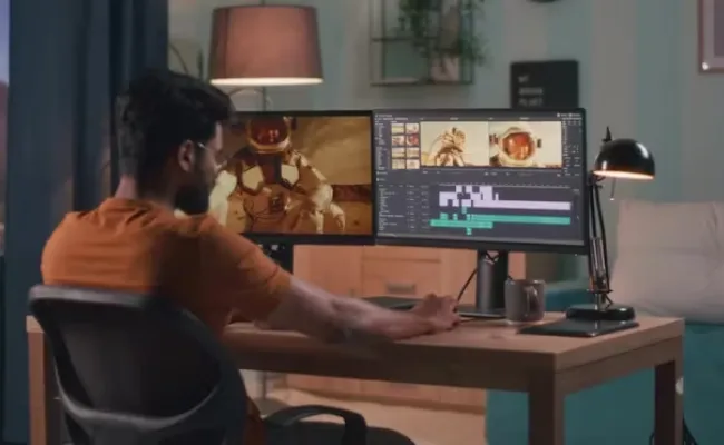 Video editor using dual monitors to edit footage and synchronize audio, applying noise reduction, mixing, and mastering as part of comprehensive video post-production services from a professional video editing company.