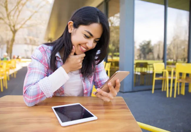 Smiling woman checking video content on her phone while seated outdoors, representing customer satisfaction and engagement with Eterna Edits’ outsourced video editing services featuring fast communication, free trials, and dedicated support.