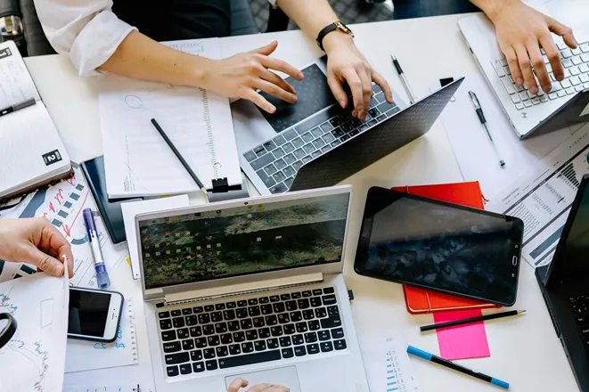 Team collaborating with laptops, tablets, and notes around a desk, illustrating improved video performance and time savings for a SaaS startup using Eterna Edits’ professional video editing services for businesses
