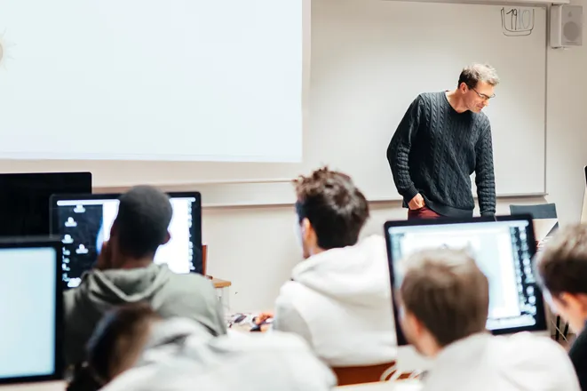 Instructor teaching in a computer lab with students at monitors, representing how Eterna Edits transformed raw class footage into high-performing social and ad content for coaching businesses through expert video editing services