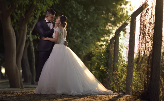 Bride and groom embracing on a tree-lined path during golden hour, illustrating the impact of professional wedding video color grading services for consistent and cinematic visual storytelling.