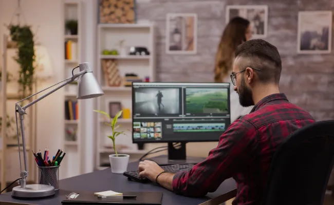 Male video editor color grading footage on dual monitors in a modern creative workspace, representing outsourced video editing services that let filmmakers focus on storytelling and production.