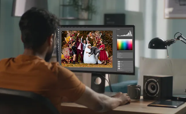 Man editing a vibrant wedding group photo on a desktop screen using professional software, showcasing expert wedding and event photo retouching for those outsourcing photography editing services.