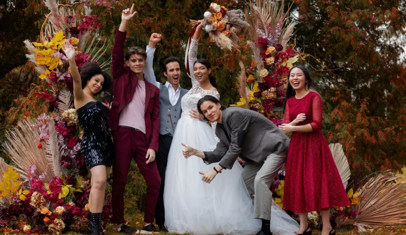 Bride and groom posing playfully with friends in front of a colorful floral arch, capturing a fun and emotional wedding moment ideal for pairing with great wedding video songs