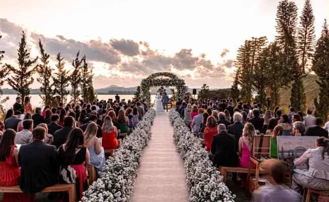 Romantic outdoor wedding ceremony at sunset with a bride and groom at the altar, surrounded by floral decorations and a large seated crowd, symbolizing the emotional moments captured by wedding videographers before post-production editing.