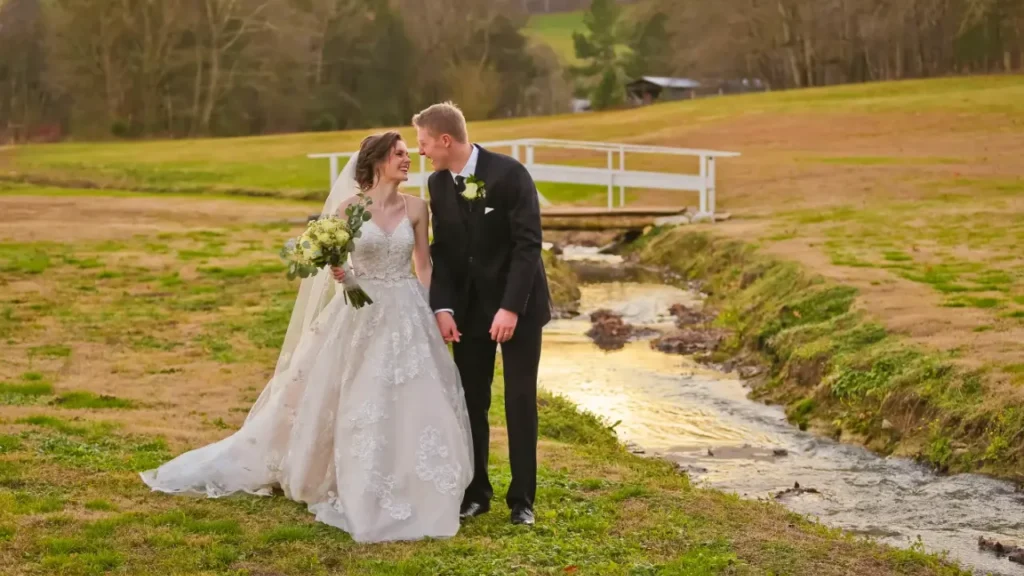 Bride and groom smiling and walking beside a scenic creek at sunset, capturing a romantic and emotional moment typical of a cinematic wedding feature film.