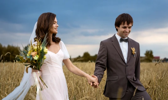 Bride and groom walking hand in hand through a field, showcasing cinematic color correction and wedding film editing services.
