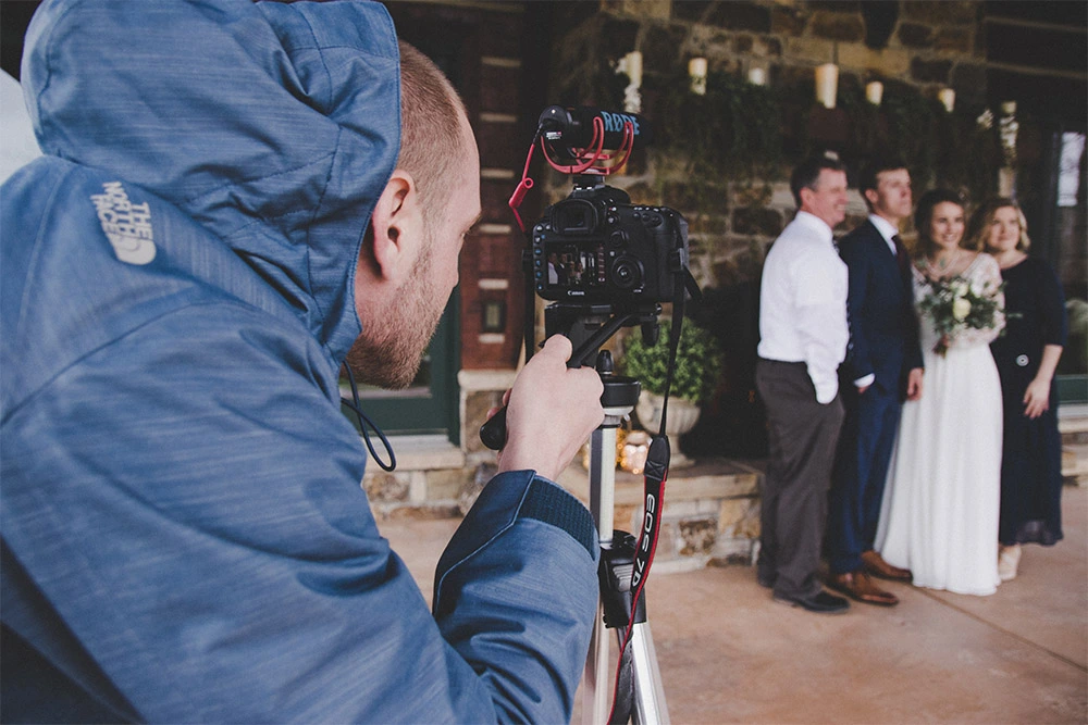 Wedding videographer filming a bride and groom with a DSLR camera, illustrating the challenge of creating a cinematic wedding highlight film from limited footage.
